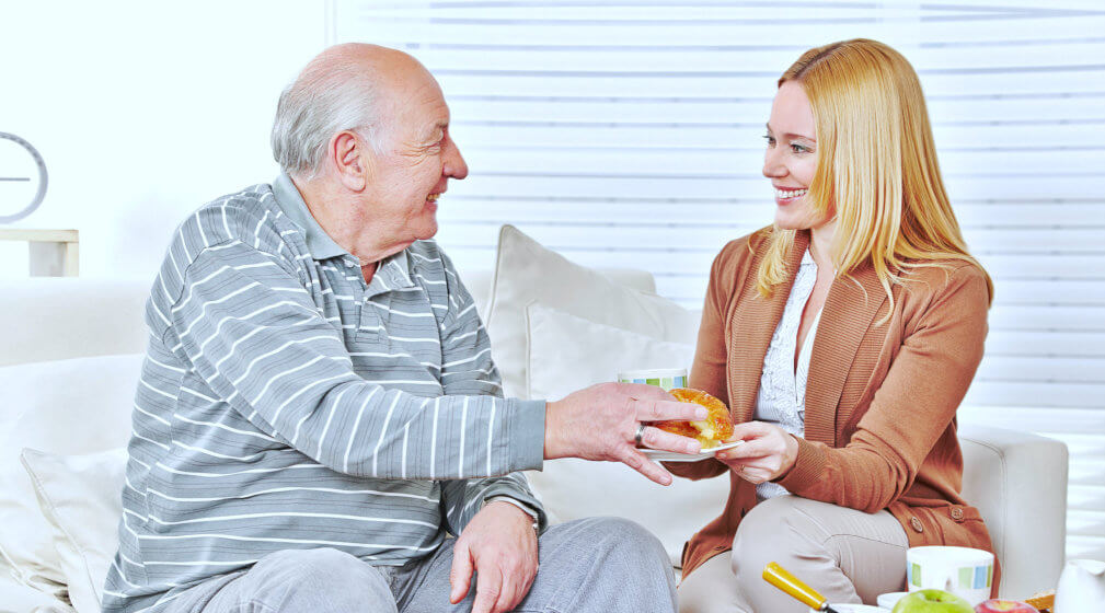 caregiver giving breakfast to an old man
